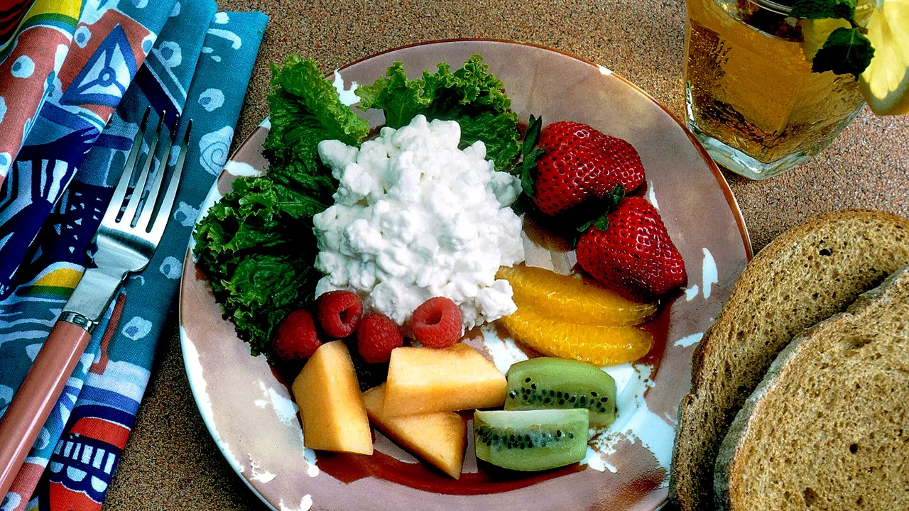 Title Healthy Snack Description A brown-beige-white plate sits on a sand-colored table. On the plate is lettuce with cottage cheese, strawberries, kiwi fruit, c