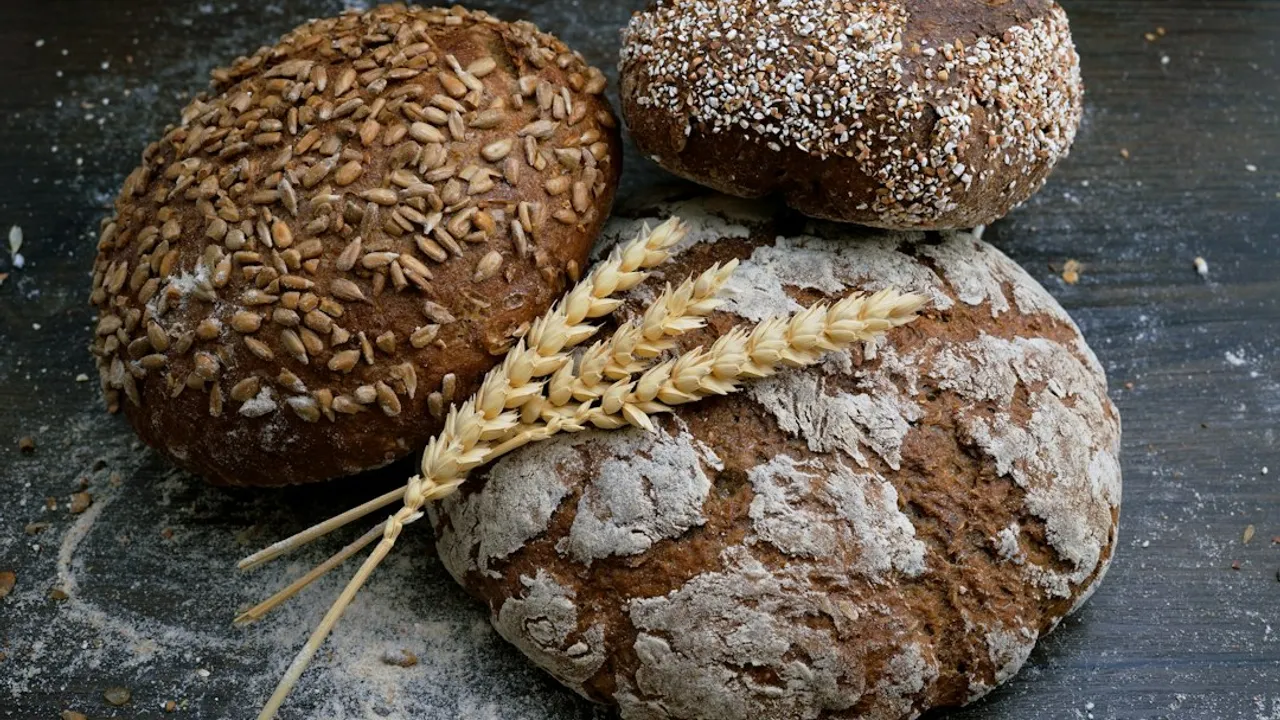 Three loaves of rustic bread with sunflower seeds and wheat stalks on wood