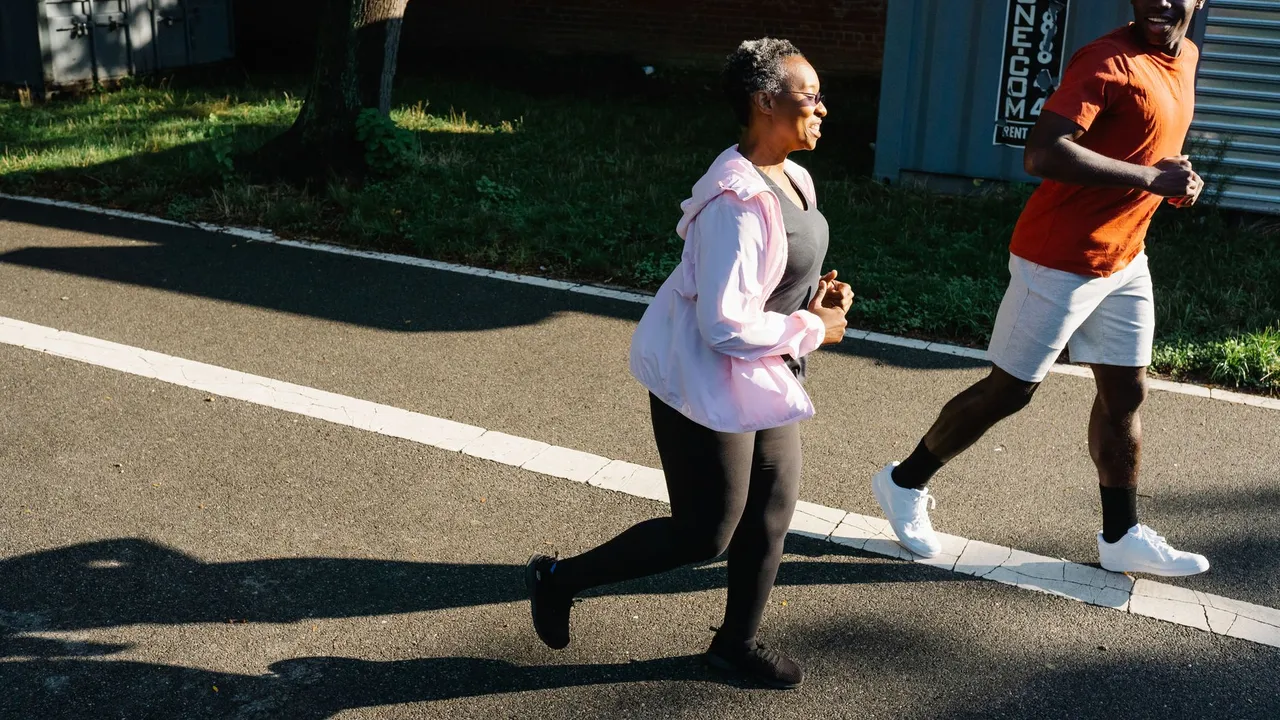 Side view of young African American man in earphones and sportswear listening to music and stretching body while performing standing forward bend exercise on st