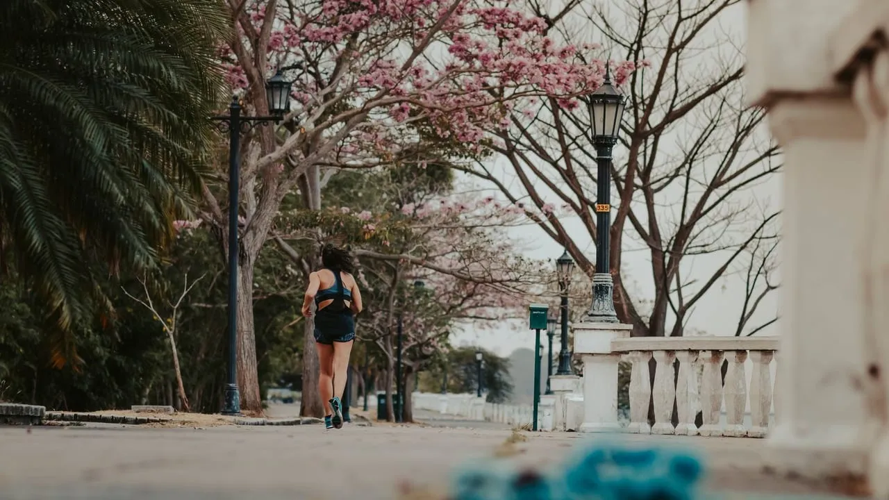 A woman jogs through a picturesque park lined with blooming spring trees and vintage lamps.