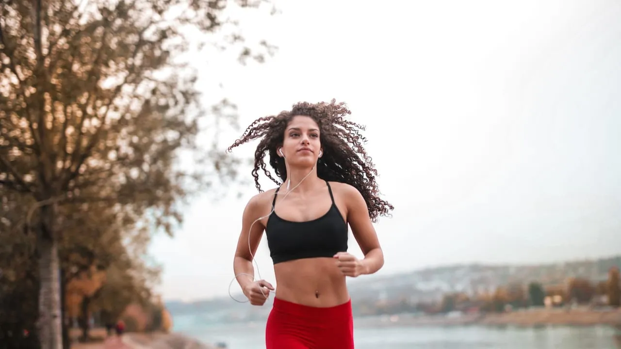 Determined woman in red leggings jogging along a scenic riverside path, embracing fitness outdoors.