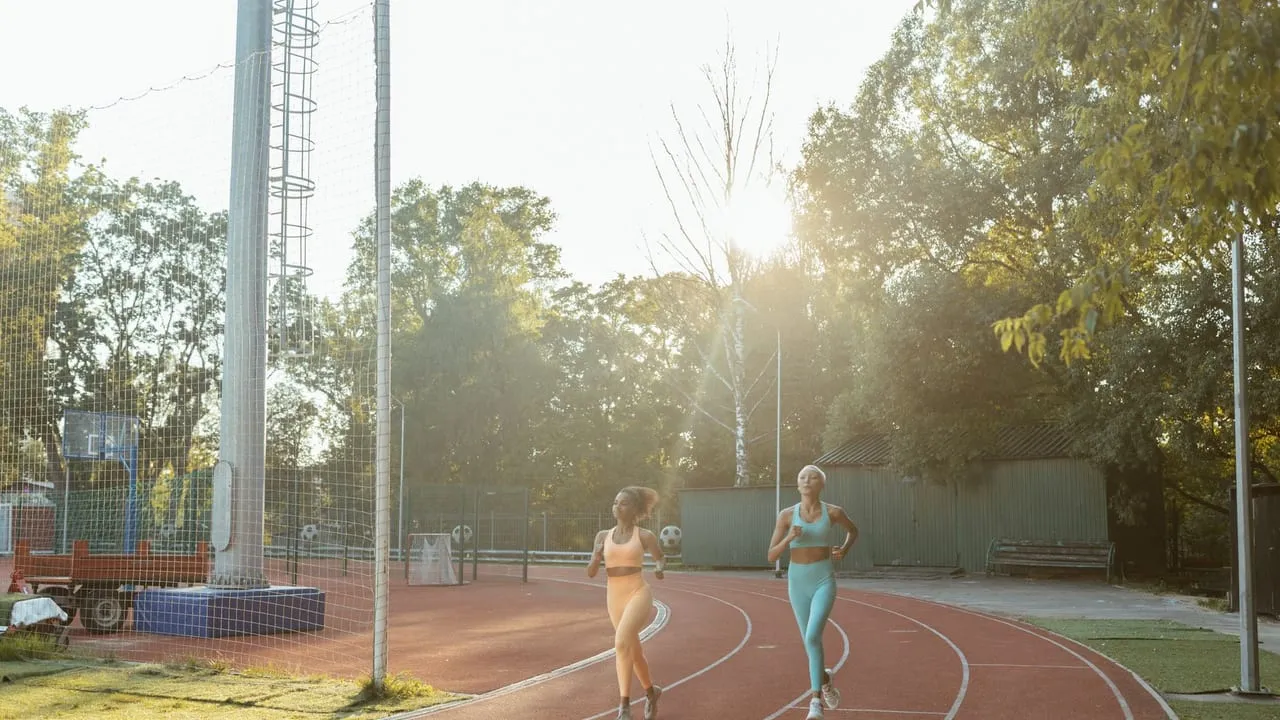 Two women jogging on an outdoor track, enjoying exercise and fitness in the morning sun.