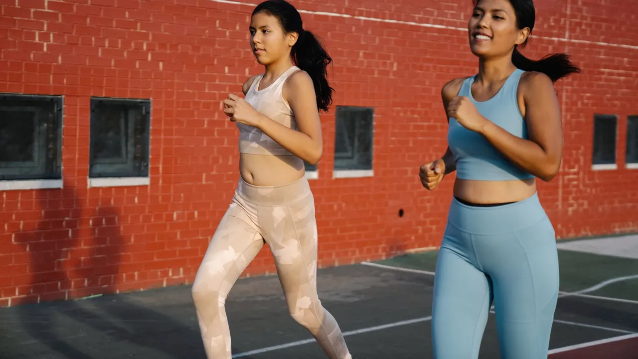 Two young women jogging outdoors in activewear, promoting fitness and healthy living.