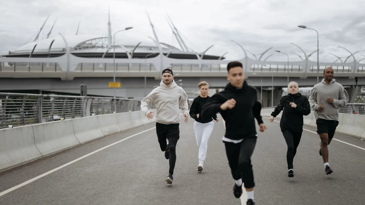 A group of diverse adults jogging on an urban road next to a modern stadium.