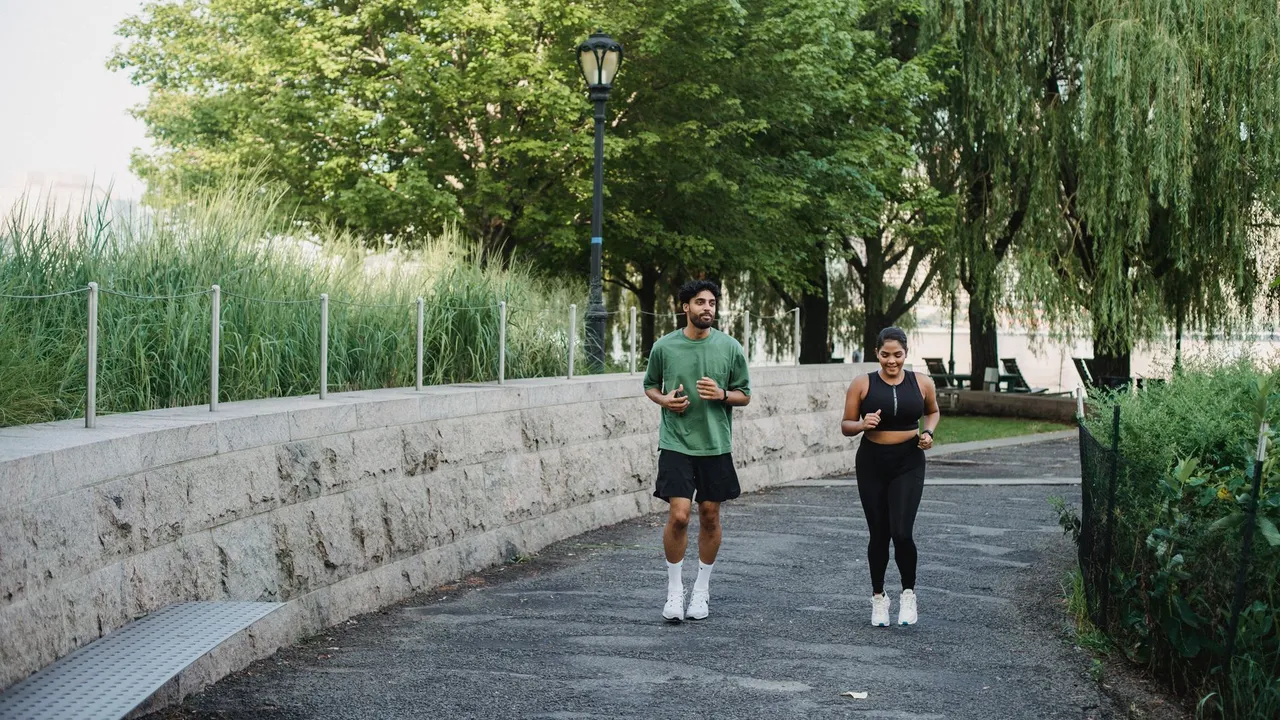 A man and woman jogging together in a lush, green park during the day.