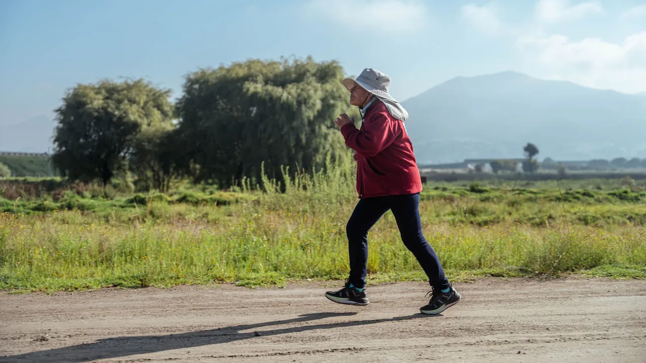 A woman in sportswear jogs along a rural road, surrounded by lush countryside and mountains.