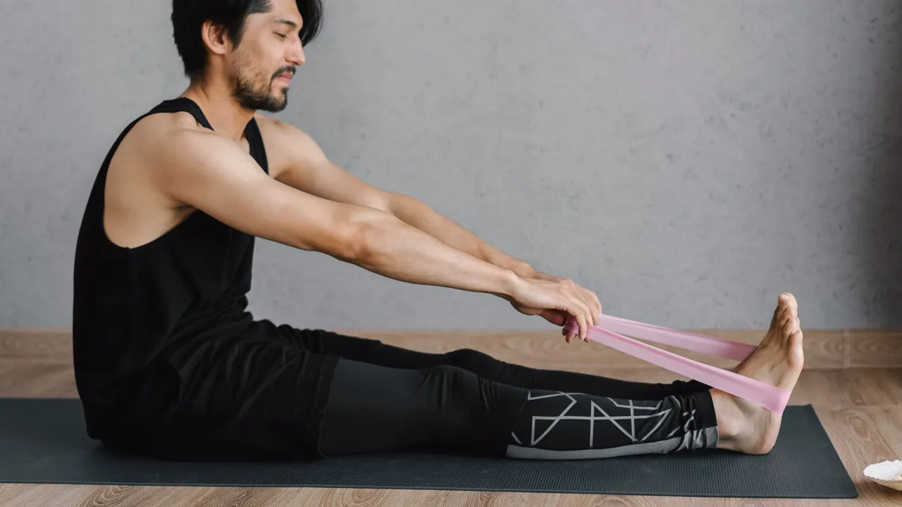 Adult man performing stretching exercises with a resistance band on a yoga mat indoors for fitness and wellness.