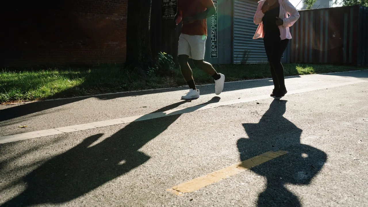 Two adults jogging on a sunlit sidewalk, casting distinct shadows.