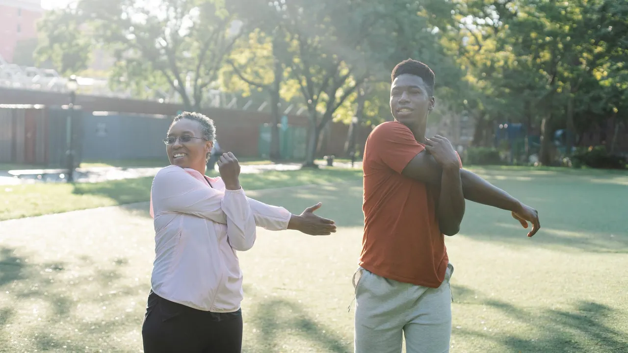 Two diverse adults stretching in a sunny park, embracing a healthy lifestyle.