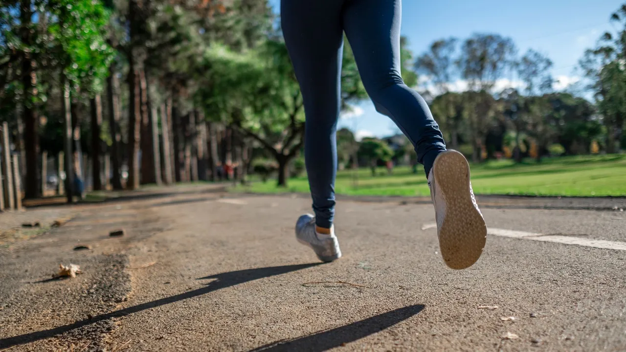 A woman running outdoors on a sunny day along a scenic park trail, focusing on fitness and health.