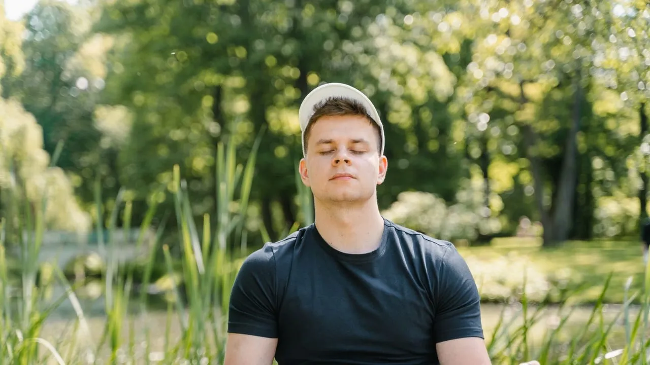 Man in black shirt meditates peacefully in a lush green park, eyes closed in relaxation