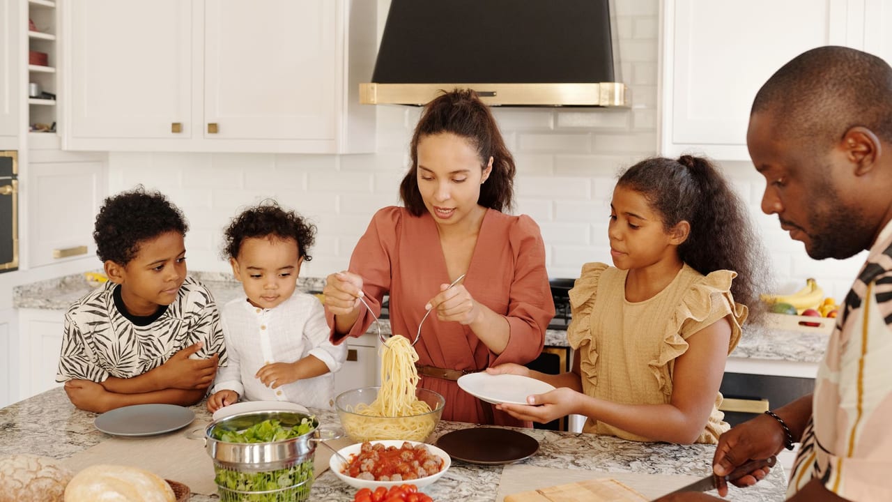 Family enjoying a cooking session together in a modern kitchen, preparing pasta and vegetables.