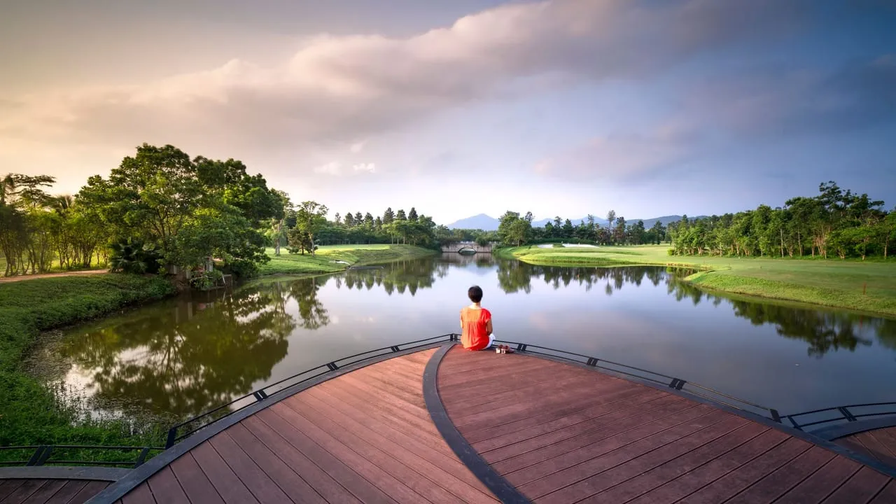 A serene scene of a person sitting by a lake, reflecting nature's beauty at sunrise.