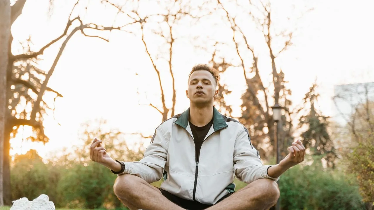 Young man meditating on a yoga mat in a serene park setting during the day.