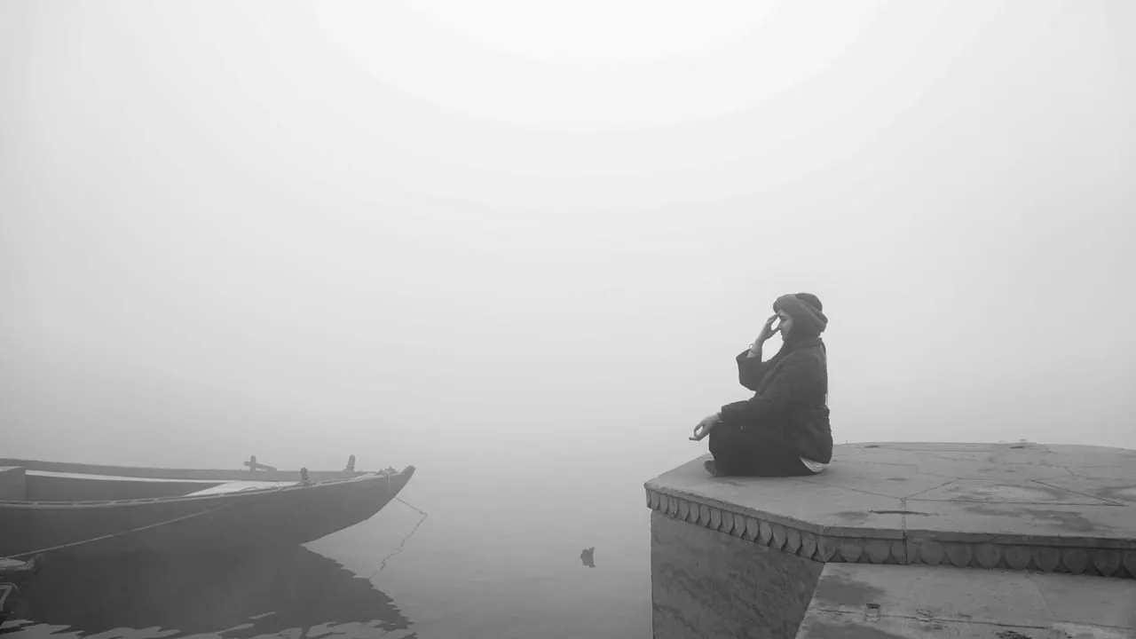 A person sits by a foggy river, exuding calm and introspection.