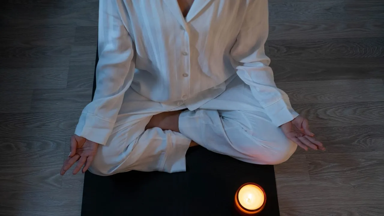 Serene meditation scene with a person in white pajamas and a glowing candle for relaxation.