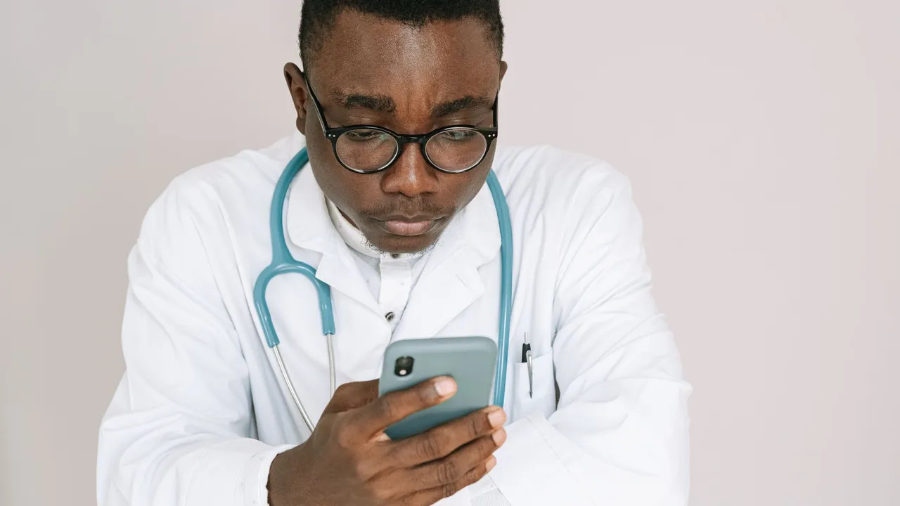 A serious male doctor in medical gown carefully reading a smartphone.