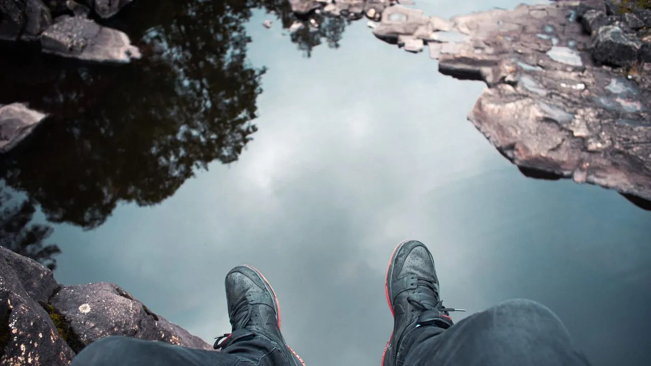 High angle view of a person sitting by water, wearing sneakers, embracing nature's tranquility.