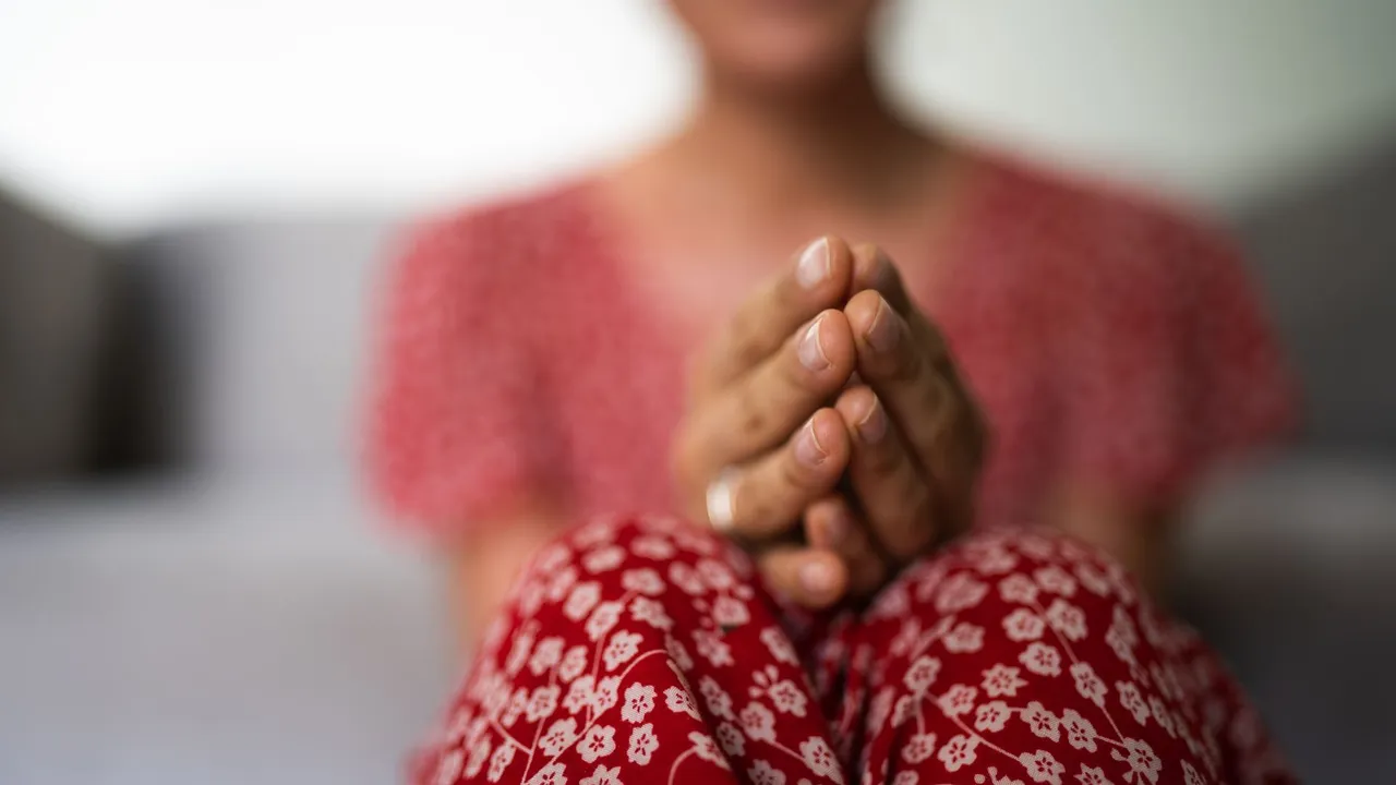 Close-up of a person in a floral dress with hands in prayer, soft focus.