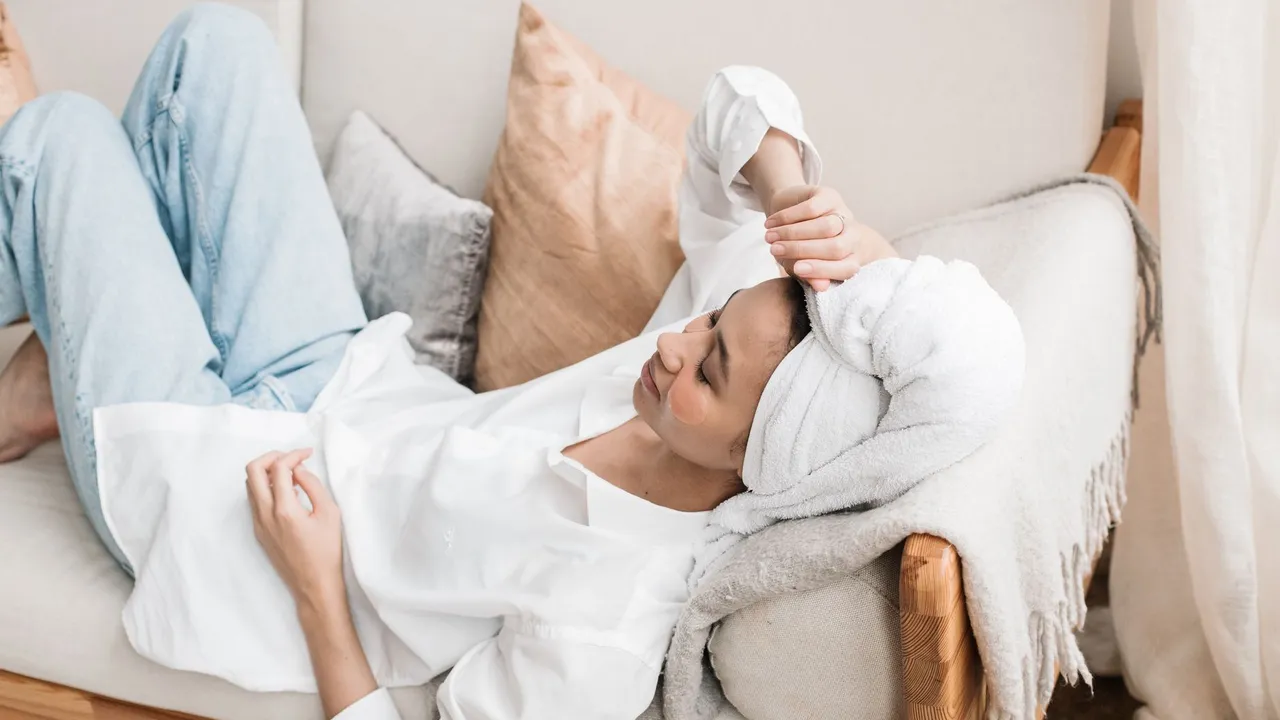 Calm woman in white shirt with a towel on her head relaxing on a comfortable sofa at home.