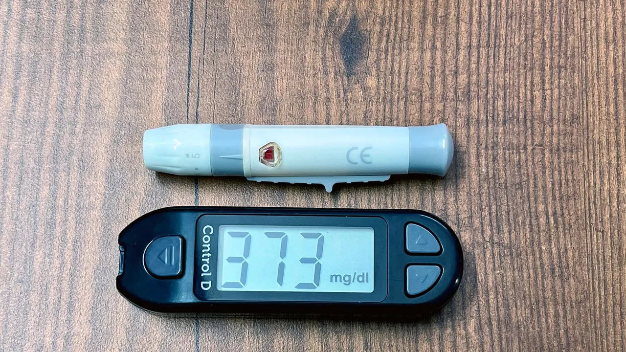 A digital glucometer and lancing device on a wooden surface indicating high blood glucose level.