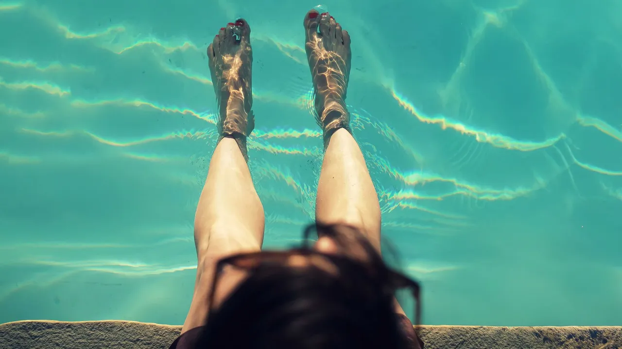 Woman relaxing with feet dipped in a clear pool on a sunny day, capturing a refreshing moment.