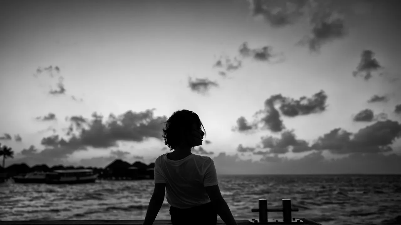 Silhouette of a woman sitting on a dock, gazing at the sunset over a calm sea.