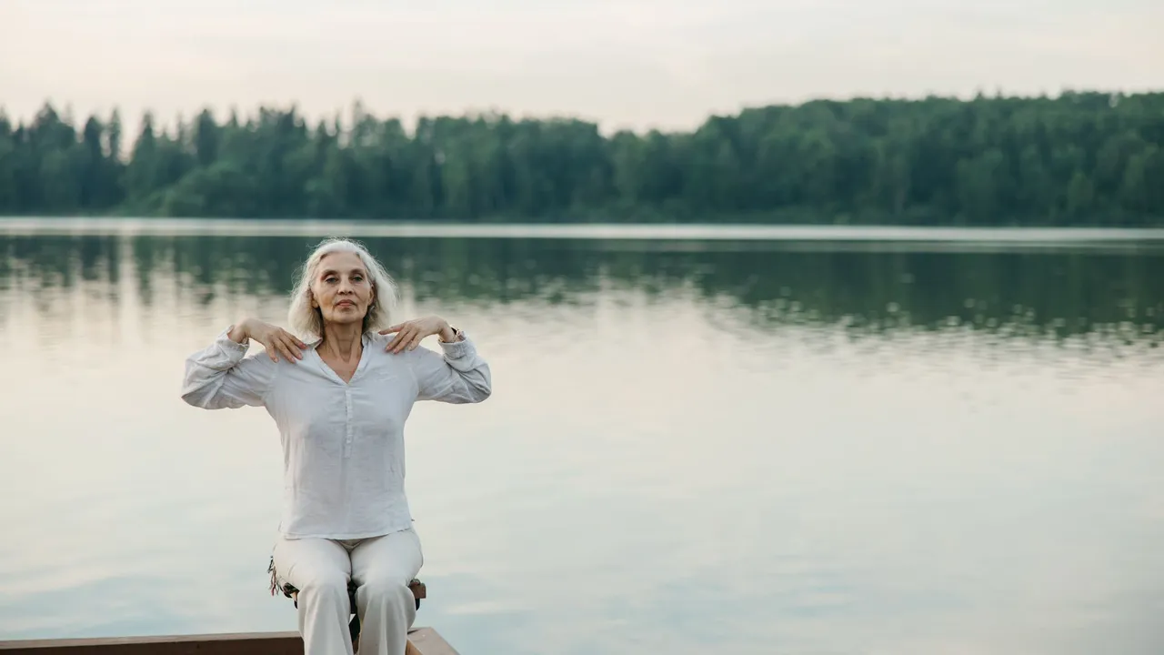A senior woman practicing yoga by a serene lake, promoting healthy aging.
