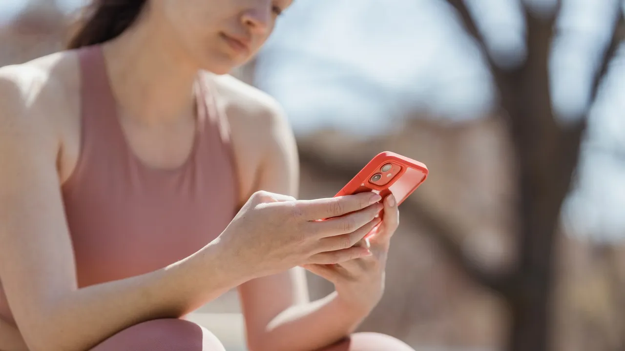 Woman in workout attire checking smartphone outdoors, enjoying a sunny day.