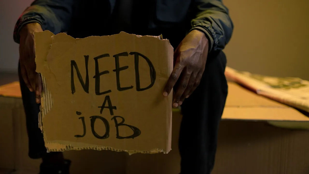 A man holding a cardboard sign reading 'Need a Job', symbolizing unemployment and hardship.